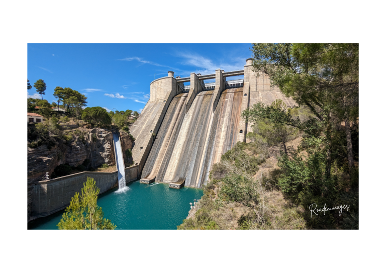 Au pied du barrage Barrage avec chute d'eau, entouré de verdure et d'eau turquoise.