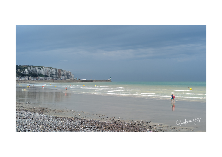 Orage à Mers les Bains Plage avec des vagues calmes, deux personnes marchant près de la mer sous un ciel orageux.