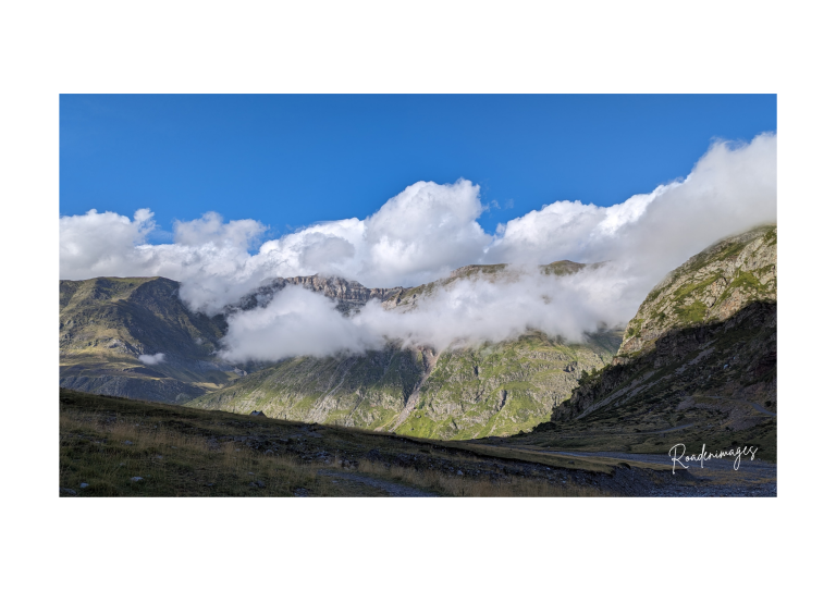 Paysage de montagne avec des nuages bas et un ciel bleu clair.