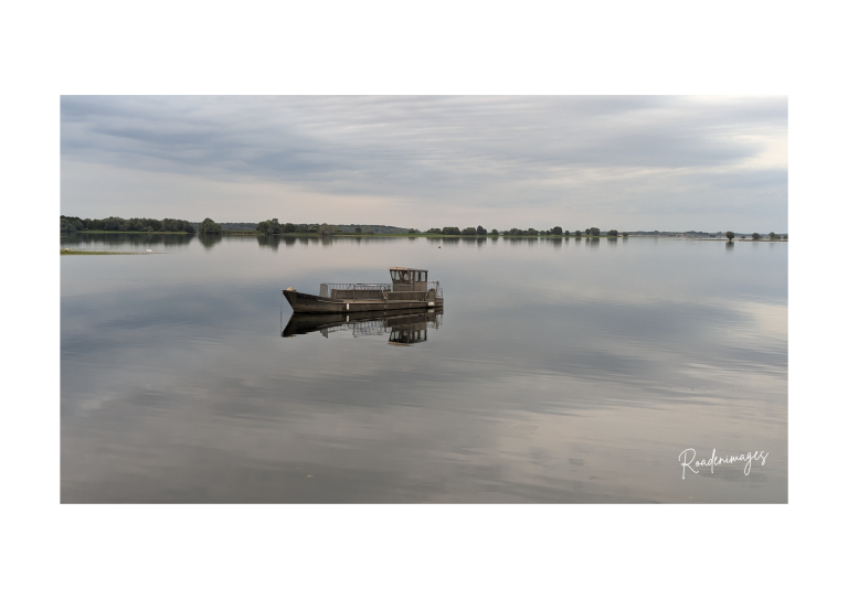 Bateau seul sur une surface d'eau calme, reflet des nuages au-dessus.